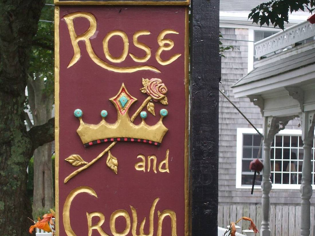 A Provincetown guesthouse sign in front of a shingled house and white picket fence