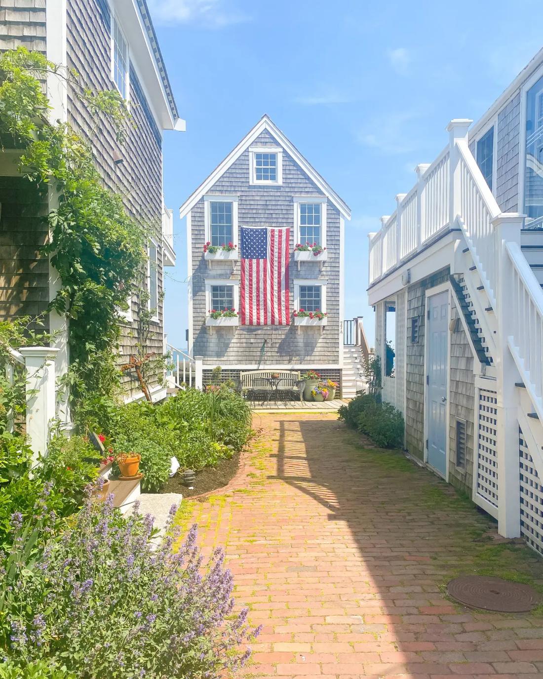 A shingled Provincetown house at the end of a brick lane, flag hung between the windows