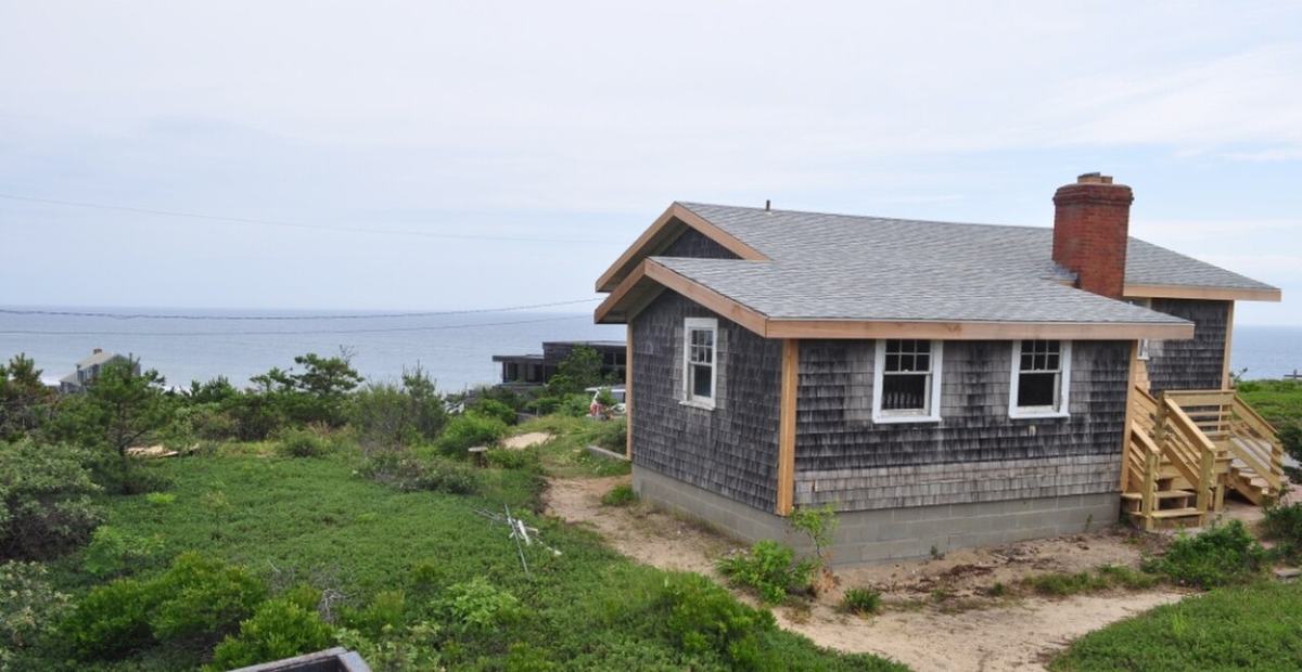 A shingled Cape Cod house on a bluff looking out over the ocean